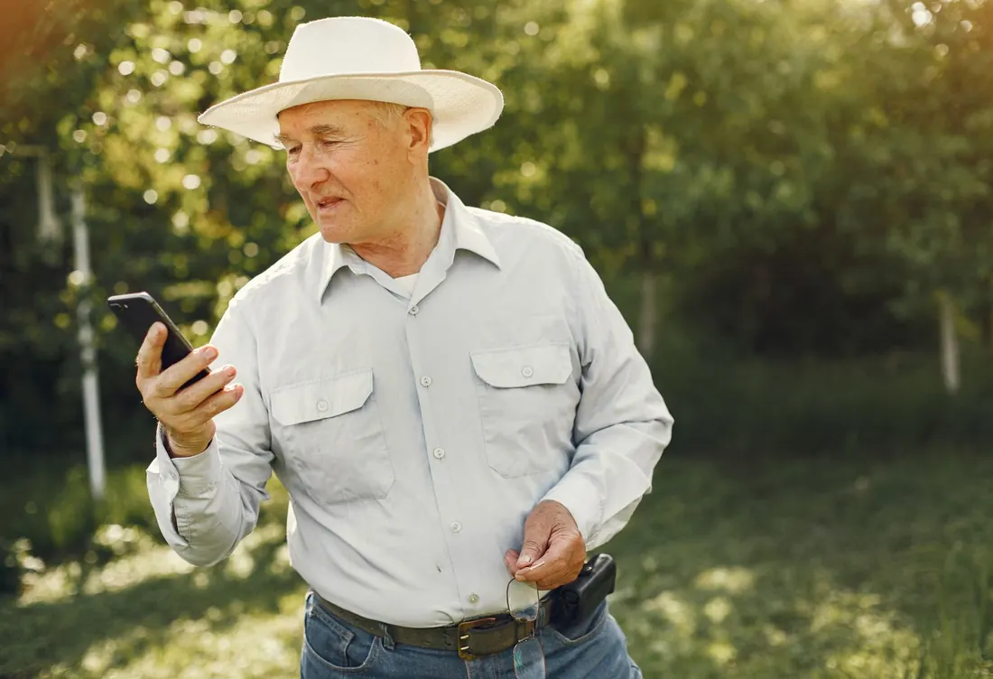 Homme âgé en chapeau regardant son téléphone en plein soleil