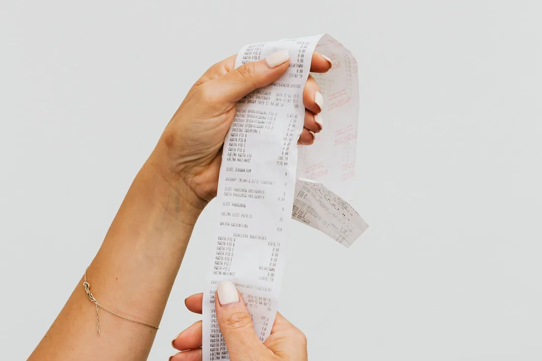 Deux mains dépliant un long ticket détaillé, comme un devis de site internet à décomposer